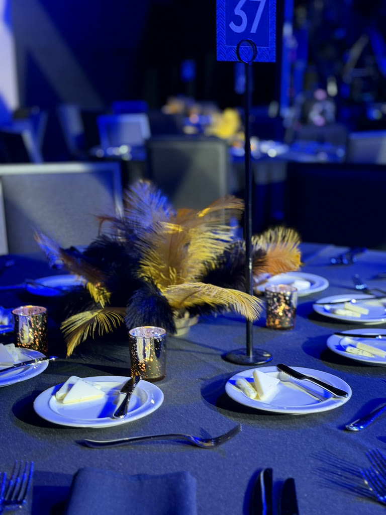 Navy and gold feather centerpiece on a blue-lit banquet table