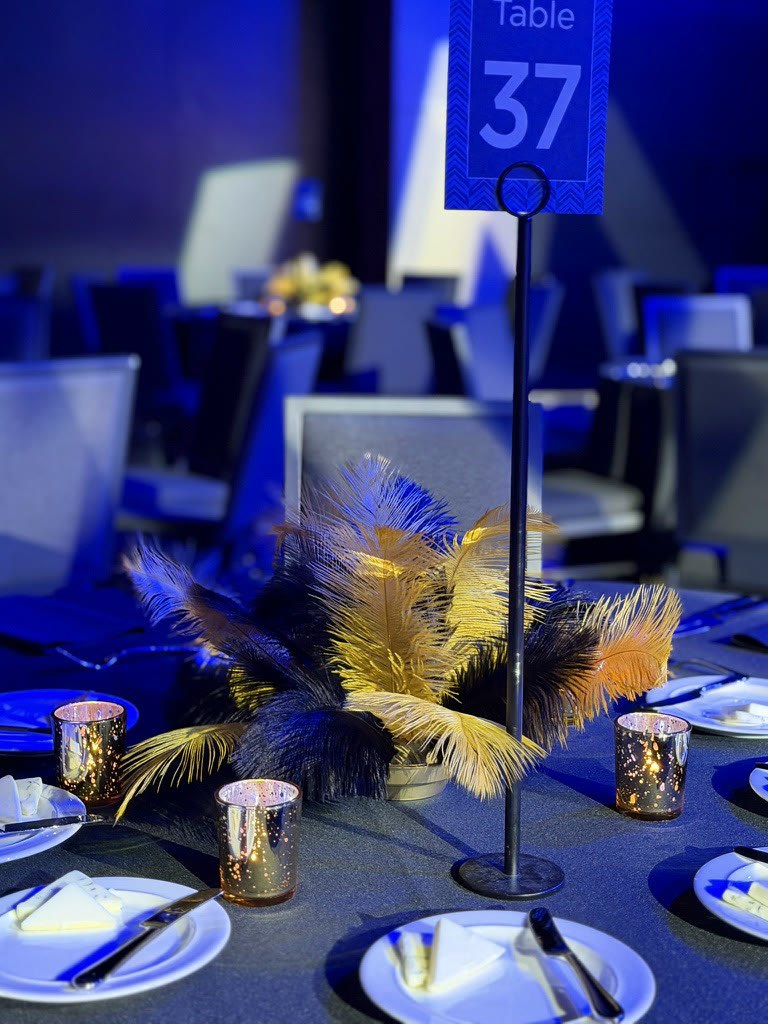 Navy and gold feather centerpiece on a blue-lit banquet table