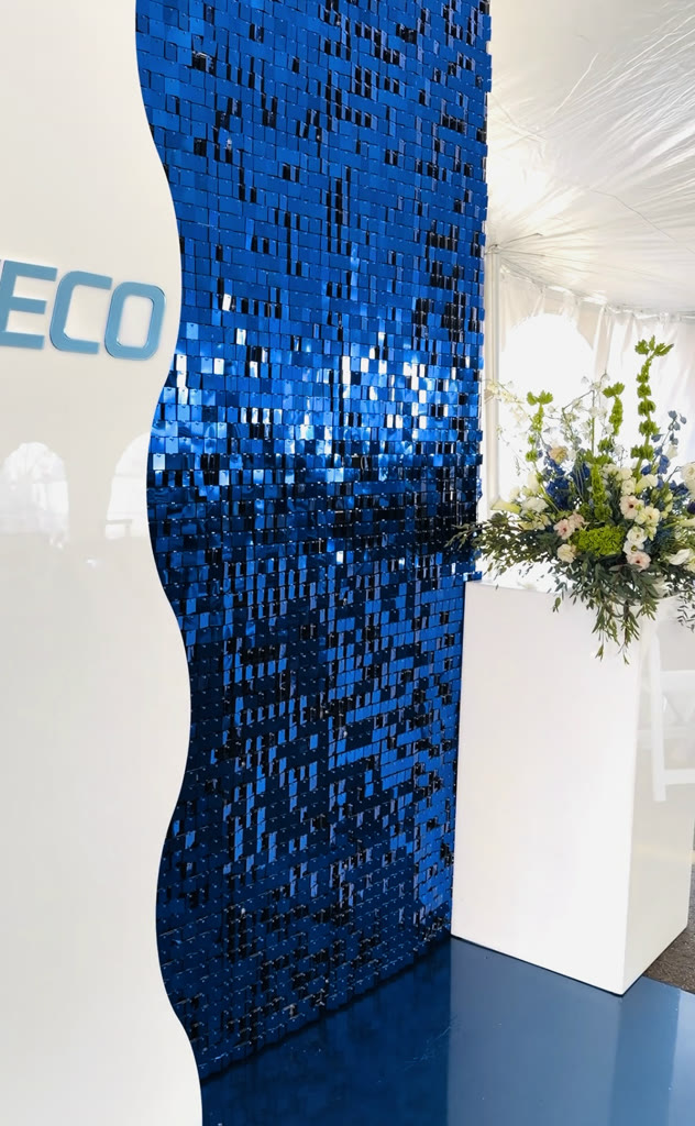 Blue sequin wave wall beside a white plinth holding a white floral arrangement