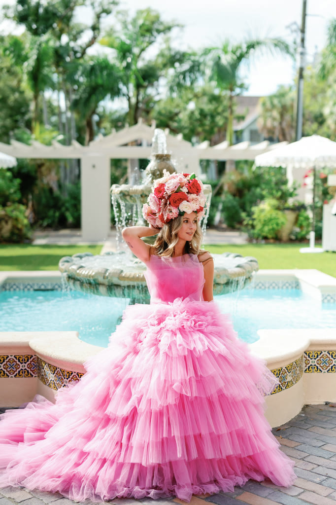 Guest in a tiered pink tulle gown and floral crown beside a courtyard fountain