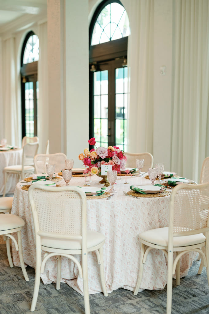 Round table dressed in blush lace with cane chairs and a pink and red floral centerpiece