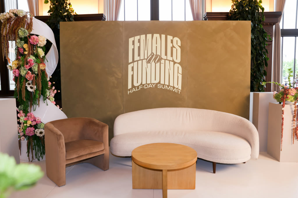 Females in Funding stage with a branded wall, curved sofa, and floral columns