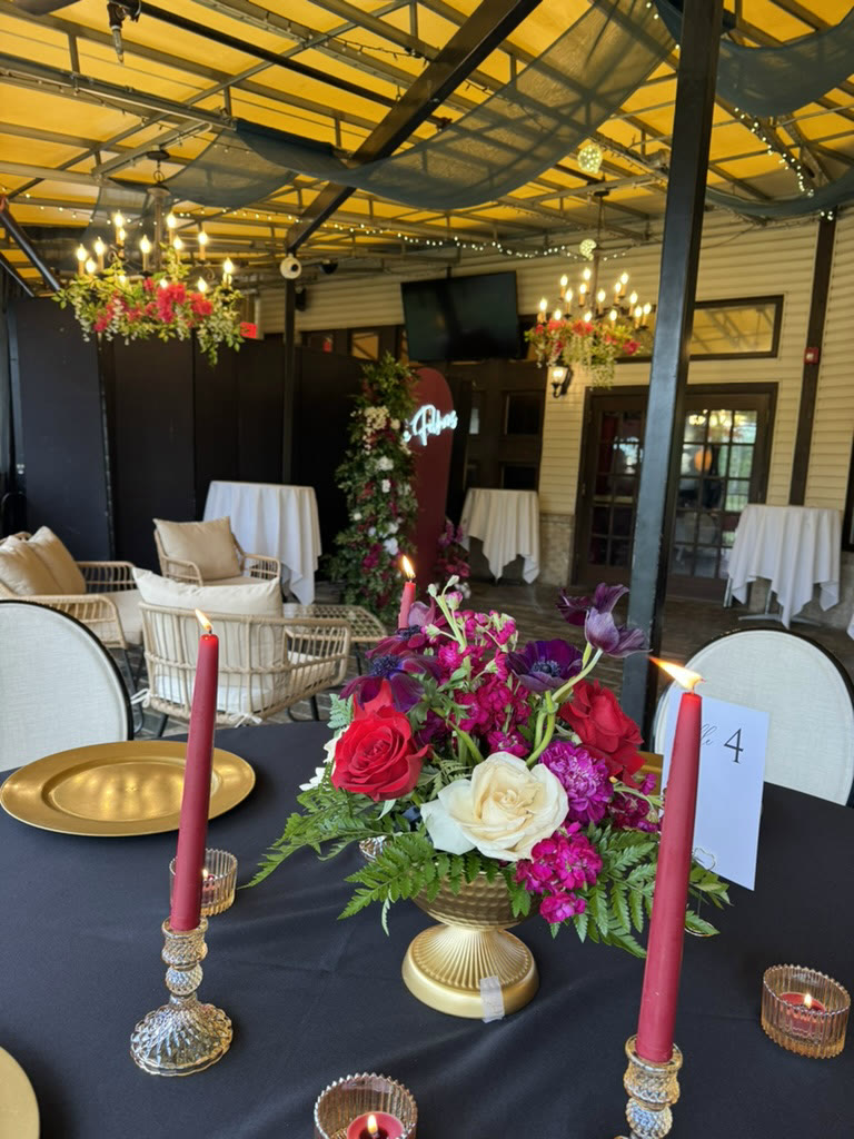 Gold charger, red tapers, and a jewel-tone centerpiece under a string-lit pergola