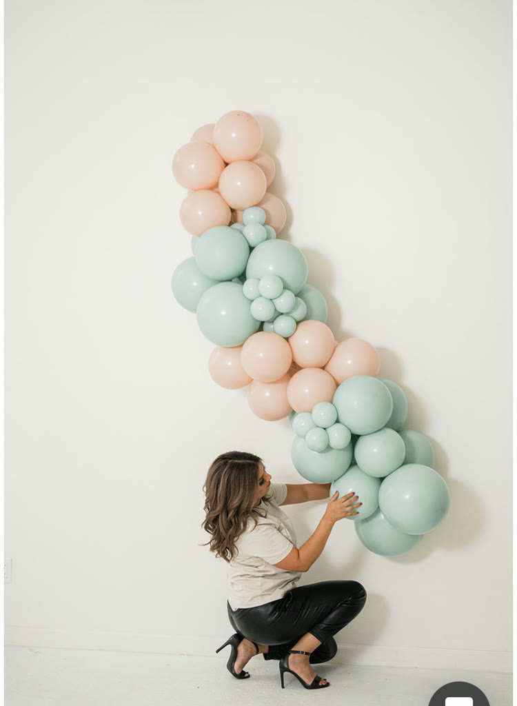 Karla Robles installing a mint and blush balloon garland on a studio wall
